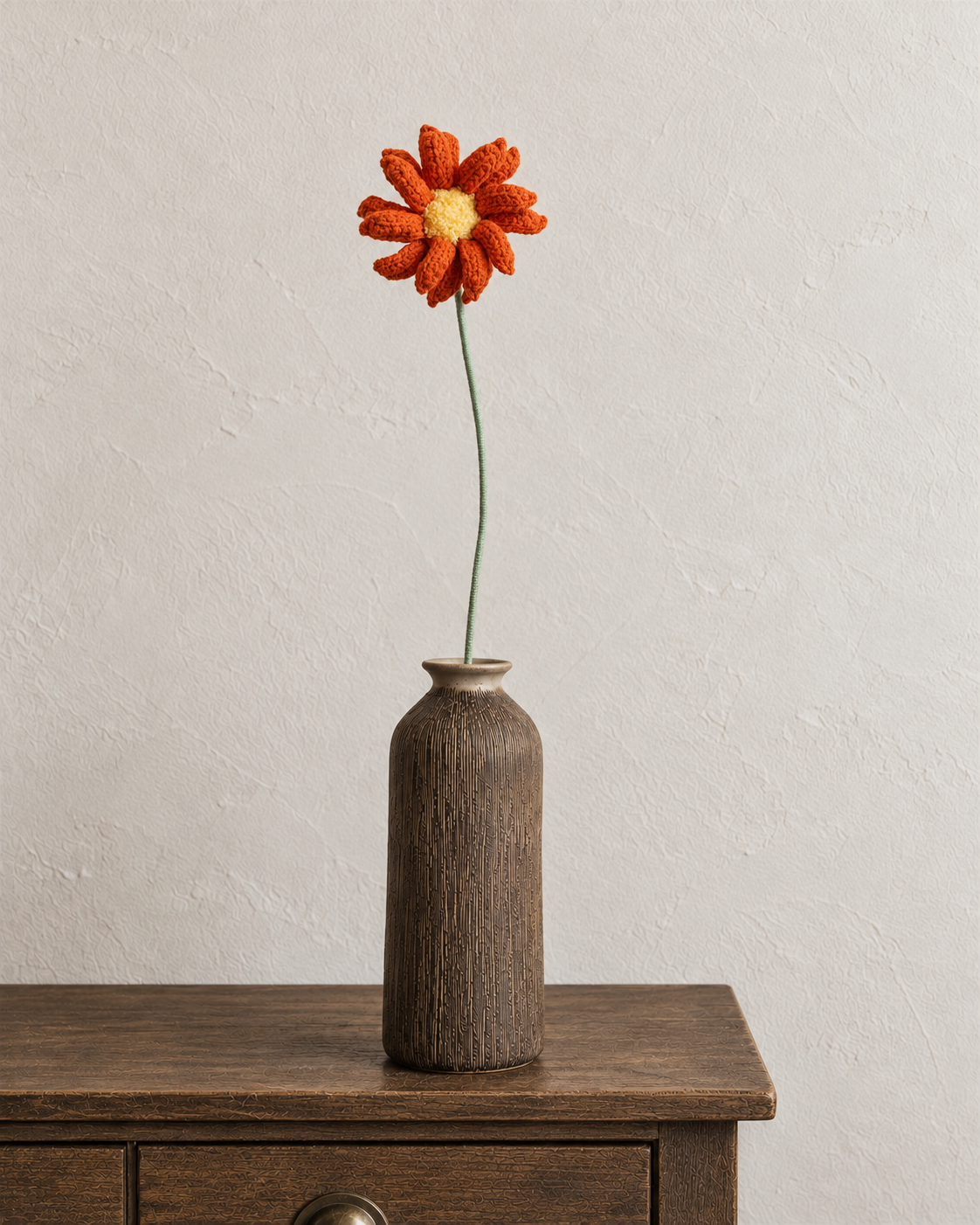 Orange crochet cosmos flower with a yellow centre in a walnut-brown textured vase; vase not included