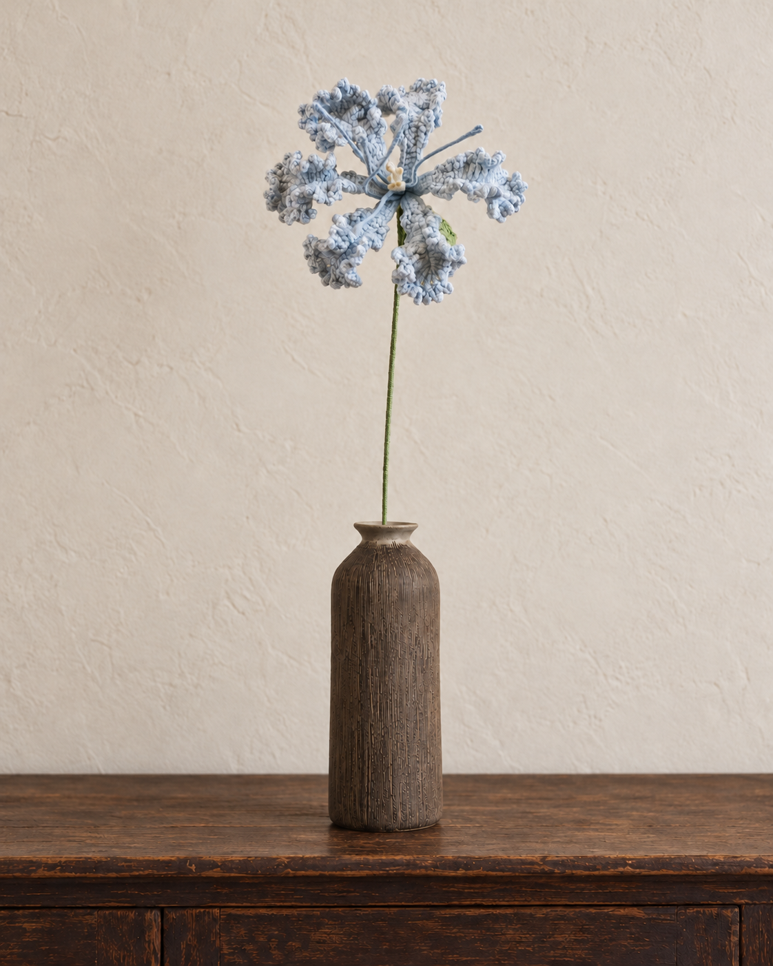 Dusty blue ruffled crochet flower in a matte walnut-brown vertically textured vase; vase not included