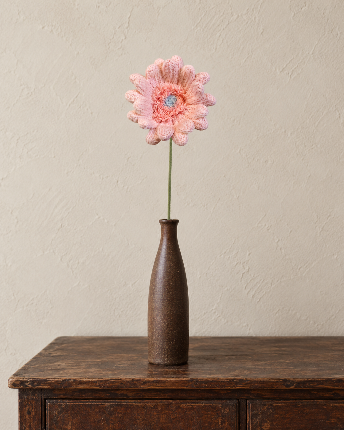 Pink handmade crochet gerbera stem styled in a slender brown vase; vase not included