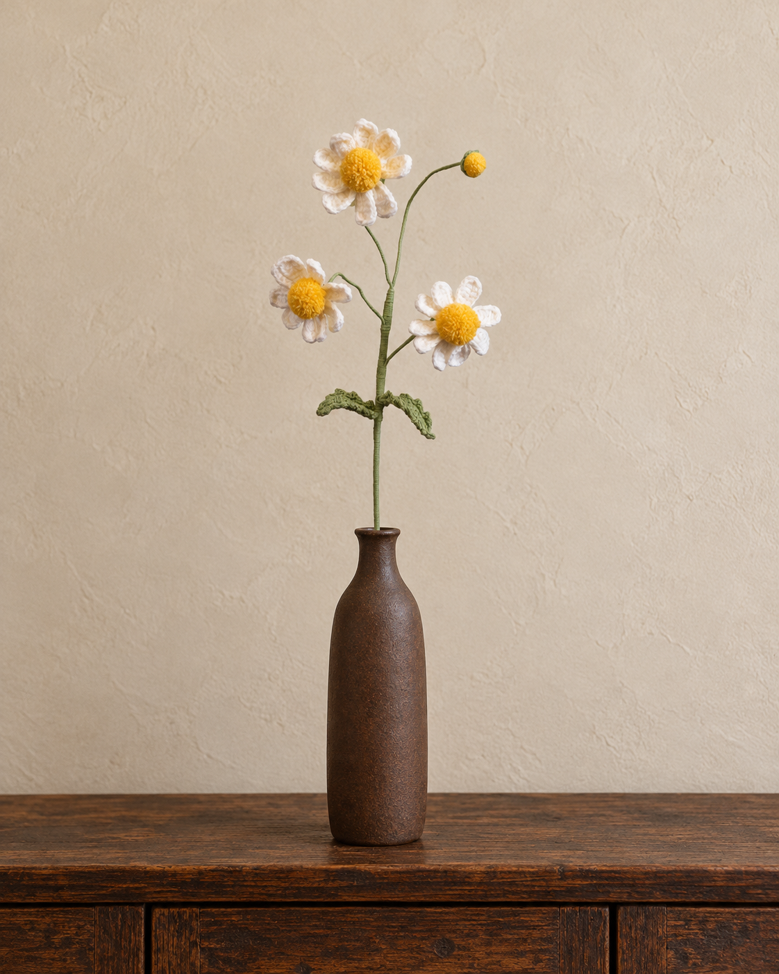Handmade crochet stem with three white daisies and one yellow bud in a slender brown vase; vase not included